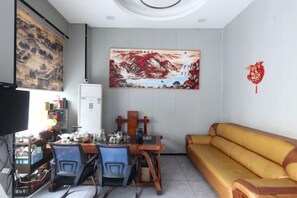 A living room with a sofa, a dining table with chairs, a TV, and artwork on the walls.