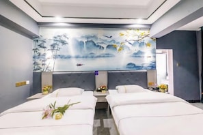 Een hotelkamer met twee bedden, een muurschildering van een landschap en een kleine tafel met bloemen.
