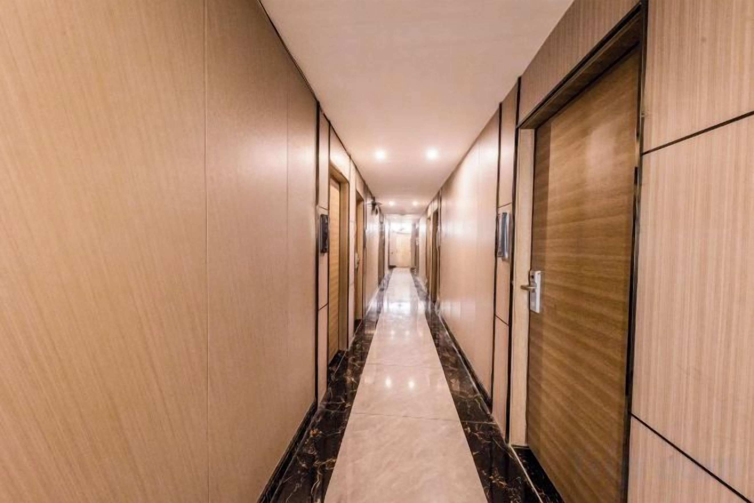 A hotel corridor with doors on both sides, a marble floor, and a wooden finish on the walls.