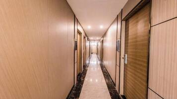 A hotel corridor with doors on both sides, a marble floor, and a wooden finish on the walls.