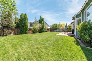 A backyard with a lawn, a wooden fence, and a house with a covered patio.