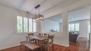 A dining area with a wooden table and benches, a hanging light fixture, and large windows with blinds. - ☀Cheerful Family Getaway ~ Large & Sunny Backyard☀ (Sparks)