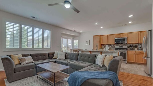 A modern living room with a sectional sofa, a coffee table, and a kitchen area with wooden cabinets and appliances. - ☀Cheerful Family Getaway ~ Large & Sunny Backyard☀ (Sparks)