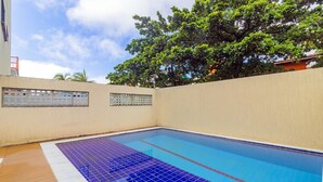 Una piscina con borde de azulejos, rodeada por un muro color beige y una terraza de madera.