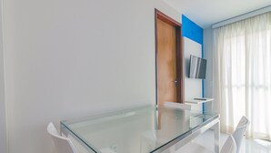 Una habitación moderna con una mesa de vidrio, sillas blancas, una puerta de madera y un televisor montado.