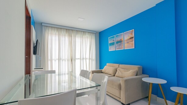 Una sala de estar moderna con una mesa de comedor de vidrio, sillas blancas, un sofá color beige y dos mesitas blancas.