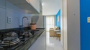 Cocina moderna con estufa a gas, un lavamanos y encimera. Hay un rincón comedor con sofá y una pequeña mesa.