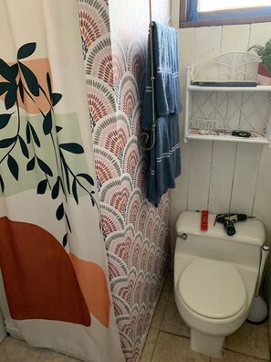 A compact bathroom with a toilet, shower, and leaf-patterned shower curtain.