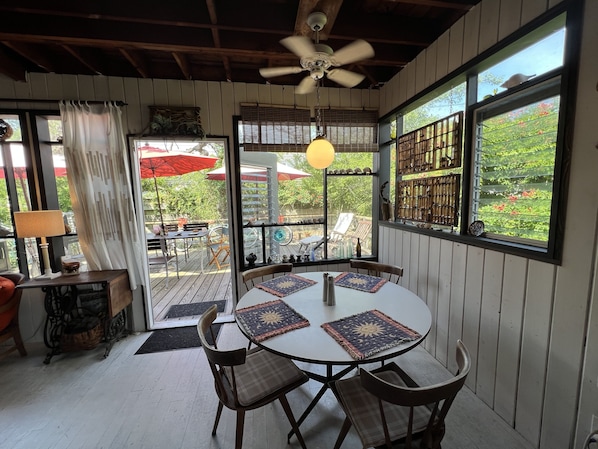 Relax in this inviting space with a round table for four, large windows offering a view of lush greenery, and a comfortable chair.
