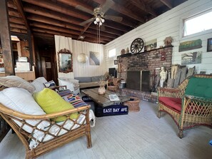 Cozy living room with a high ceiling, exposed beams, and a comfortable seating area featuring a wicker sofa and armchair.