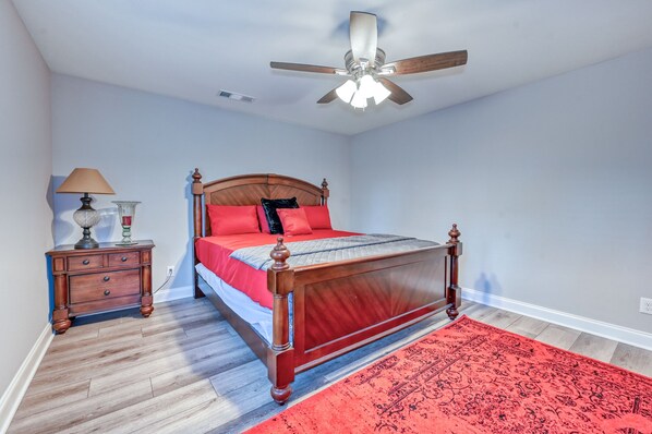Een slaapkamer met een houten bed, een nachtkastje, een lamp en een rood vloerkleed.