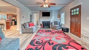 A spacious living room with a fireplace, a ceiling fan, and a large rug.