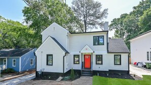 A two-story house with a red door, white siding, and a small front yard.