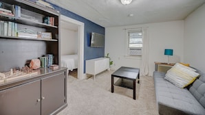 A living room with a bookshelf, a grey sofa, a small table, and a TV mounted on the wall.