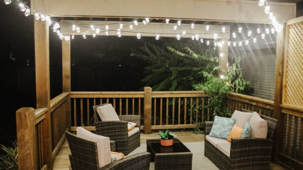 A wooden deck with wicker furniture, string lights, and potted plants. - Private Patio W/ Grill + Game Room - Sleeps 10! (Wichita)
