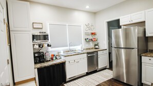 A modern kitchen with white cabinets, stainless steel appliances, and a window with blinds. - Private Patio W/ Grill + Game Room - Sleeps 10! (Wichita)