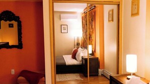 A hotel room with a wooden floor, a bed with white bedding, a nightstand with a lamp, a mirror, and a red wall. - Dream getaway apartment in the foot of Gunks Ridge (Wallkill)