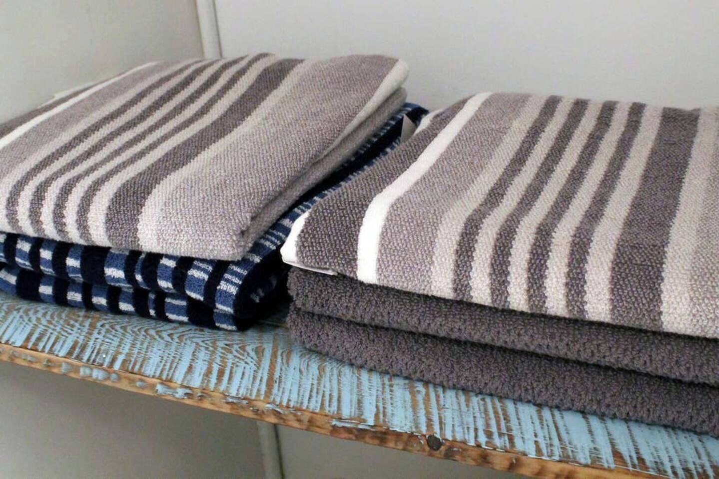 A stack of folded towels with striped patterns on a rustic wooden shelf.