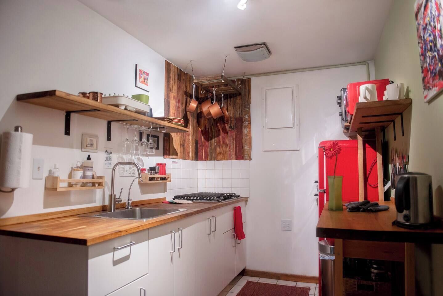 Una cocina compacta con encimeras de madera, un lavamanos de acero inoxidable y un refrigerador rojo.
