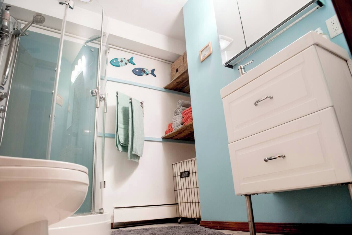 A bathroom with a glass shower enclosure, a white toilet, a towel rack with a green towel, and a white cabinet with drawers.