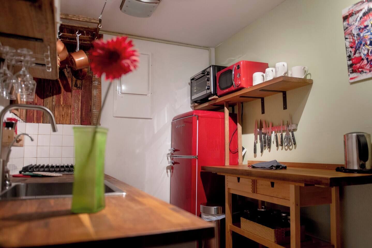 Una cocina con un refrigerador rojo, un microondas y una repisa con tazas y cuchillos.