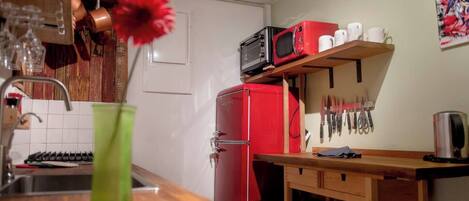 Una cocina con un refrigerador rojo, un microondas y una repisa con tazas y cuchillos.