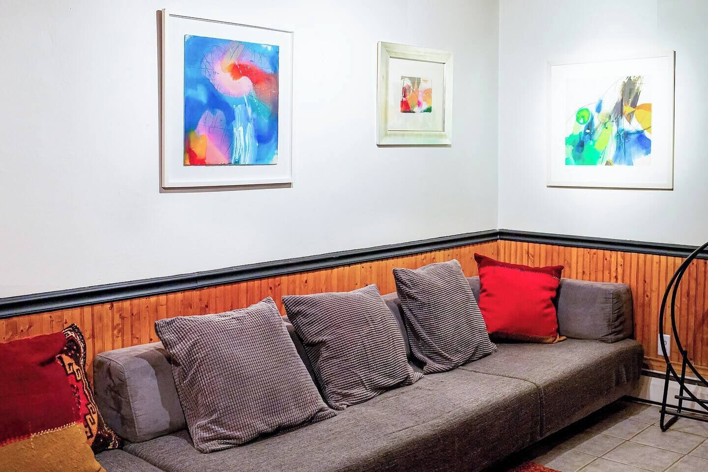 Una sala de estar moderna con un sofá gris, paneles de madera y tres pinturas abstractas en la pared.