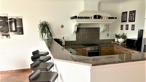 Uma cozinha moderna com uma ilha central, banquetas, fogão e micro-ondas.