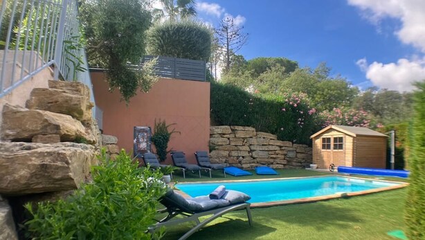 Um quintal com piscina, um pequeno galinheiro de madeira e um muro de pedra.