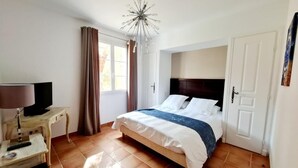 Quarto com uma cama, mesa de cabeceira com luminária, televisão e janela com cortinas.