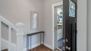 Un pasillo con una escalera blanca, una consola negra y una puerta con panel de vidrio.