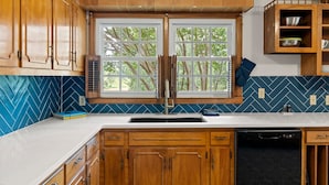 Una cocina con armarios de madera, una ventana con persianas, un fregadero y un lavavajillas.
