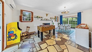 Una habitación amplia con mesa de fútbol, chimenea de ladrillo y comedor con mesa y sillas.