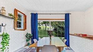 Un comedor con mesa de madera, sillas blancas, un florero con flores y vistas a zonas verdes.