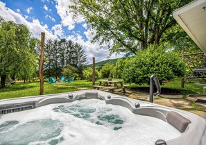 A hot tub in a backyard with a picnic table and chairs, surrounded by trees and a grassy area.