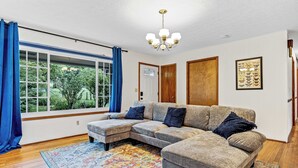 Una sala de estar con un sofá modular, una araña, un ventanal con cortinas azules y una alfombra colorida.