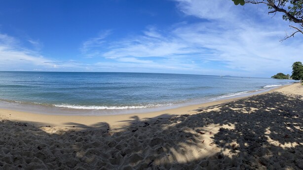 Une plage de sable fin, avec une eau d’un bleu limpide et quelques bateaux visibles au loin.