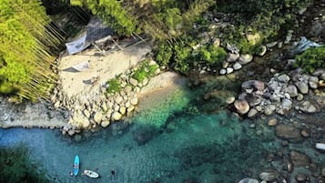 Una playa con agua cristalina, rocas y una pequeña cabaña.