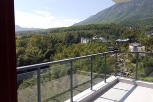 Varanda com guarda-corpo de vidro, com vista para uma paisagem montanhosa e edifícios dispersos.