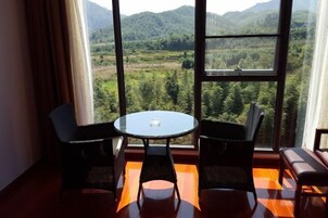 Habitación con un ventanal grande que ofrece vistas a un paisaje boscoso. En el centro, una mesa redonda con dos sillas.