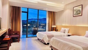 Habitación de hotel con dos camas, un escritorio, sillas, un ventanal con vistas y un cuadro en la pared.
