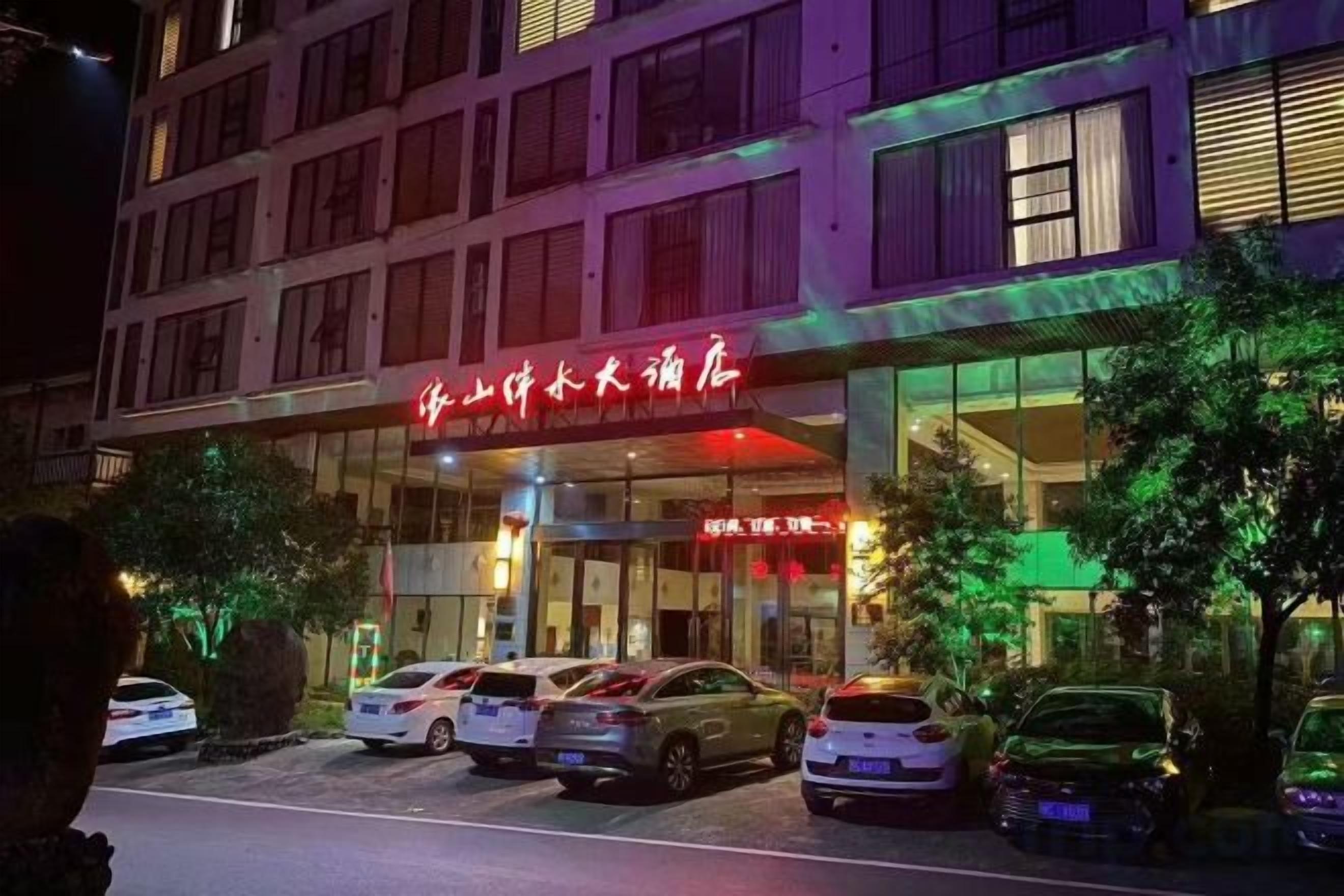 Un hotel con un letrero rojo, varios coches estacionados frente a él y un edificio con amplias ventanas.
