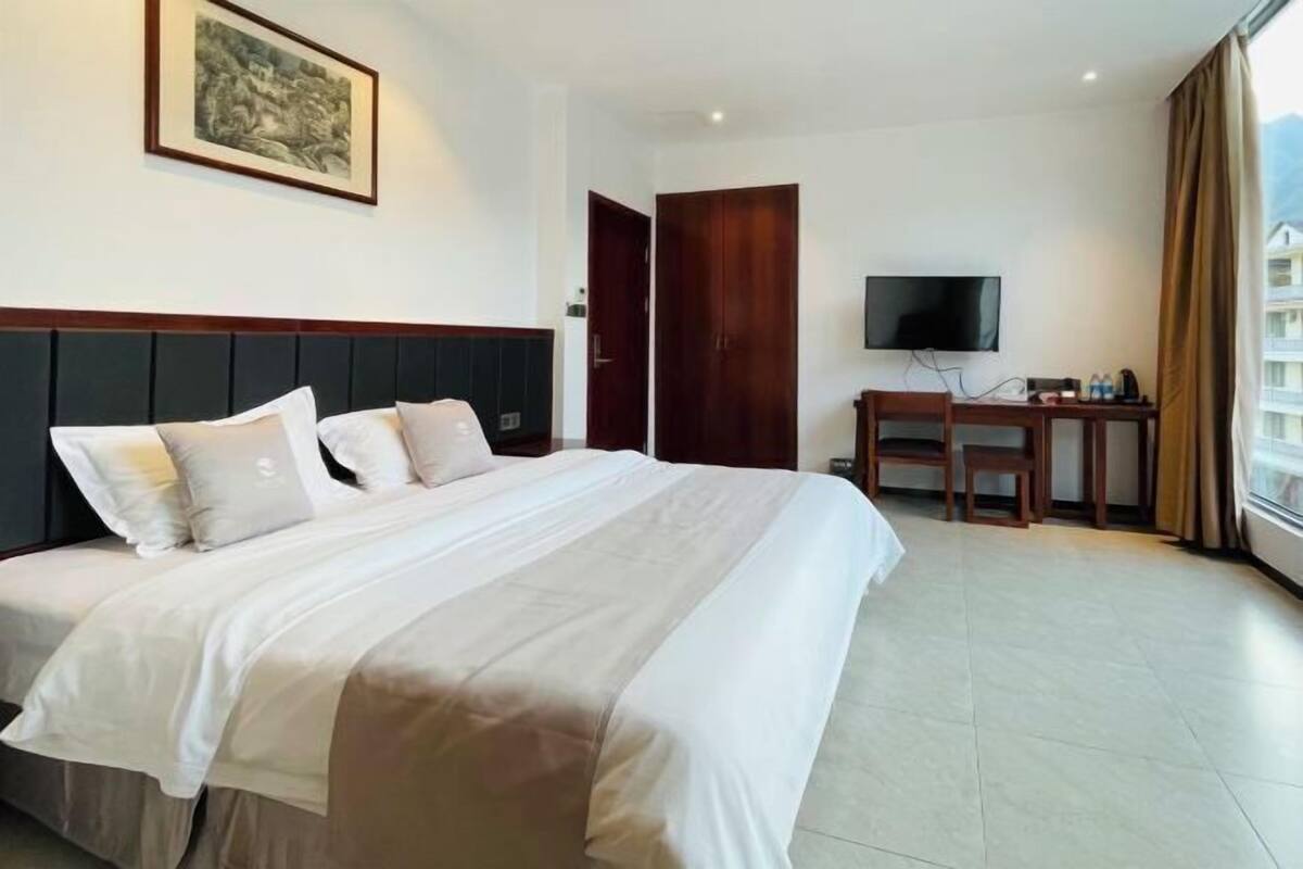 A hotel room with a bed, a TV, a desk, and a window with curtains.
