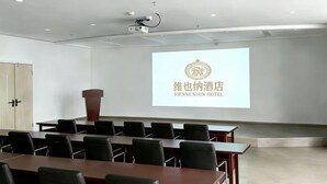 A conference room with a projection screen displaying hotel branding, a podium, and multiple tables and chairs. - Vienna Hotel (Yixing High-speed Railway Station) (Yixing)