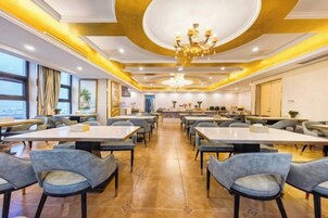 Un comedor de hotel con mesas y sillas, una araña de cristal y vistas a través de las ventanas.