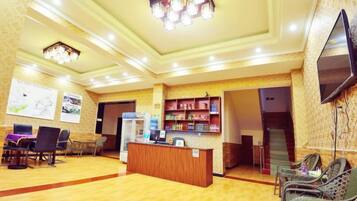 A hotel lobby with a reception desk, seating area, and a staircase leading to other floors.