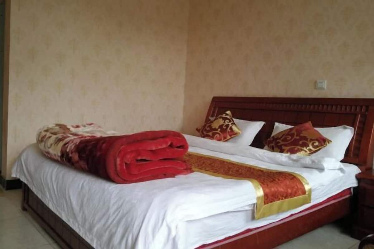 A neatly made bed with a red blanket and a decorative golden trim.