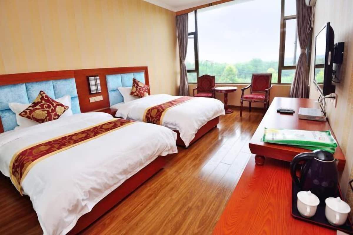 A hotel room with two beds, a desk, a chair, a television, and a window with a view.