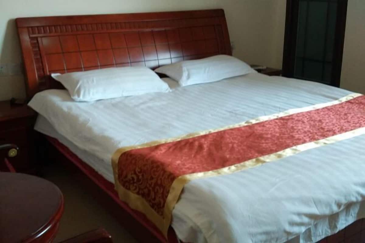 A hotel room with a wooden headboard, a bed with white linens and a red and gold bedspread, a wooden nightstand, and a round wooden table.