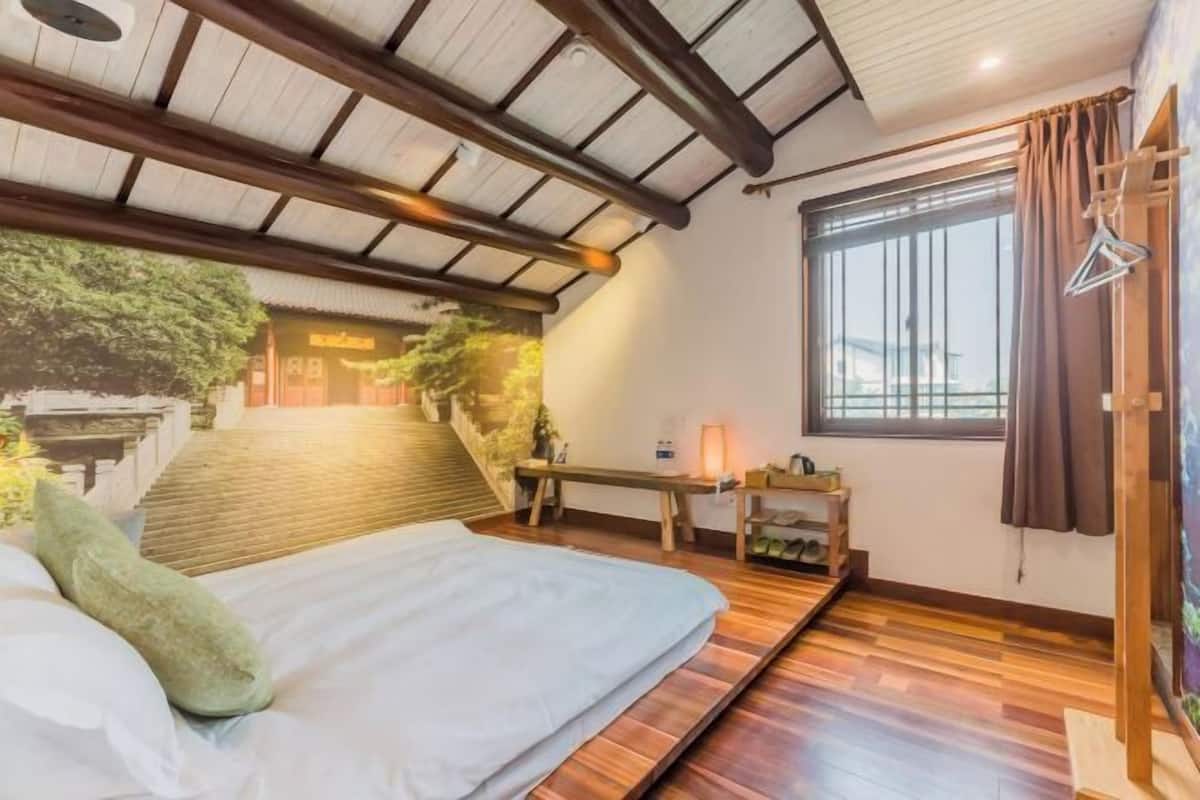 Een slaapkamer met een bed, een klein tafeltje, een raam met gordijnen en een uitzicht op een gebouw.